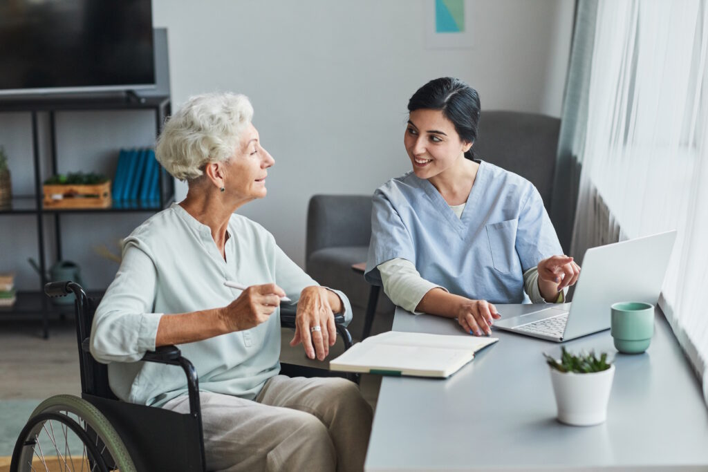 Smiling female nurse helping senior woman using laptop at home